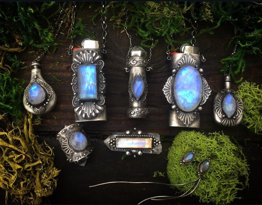 The Moonstone Collection: sterling lighter cases, phials, a cuff ring and earrings with glowing blue moonstones, arranged on moss