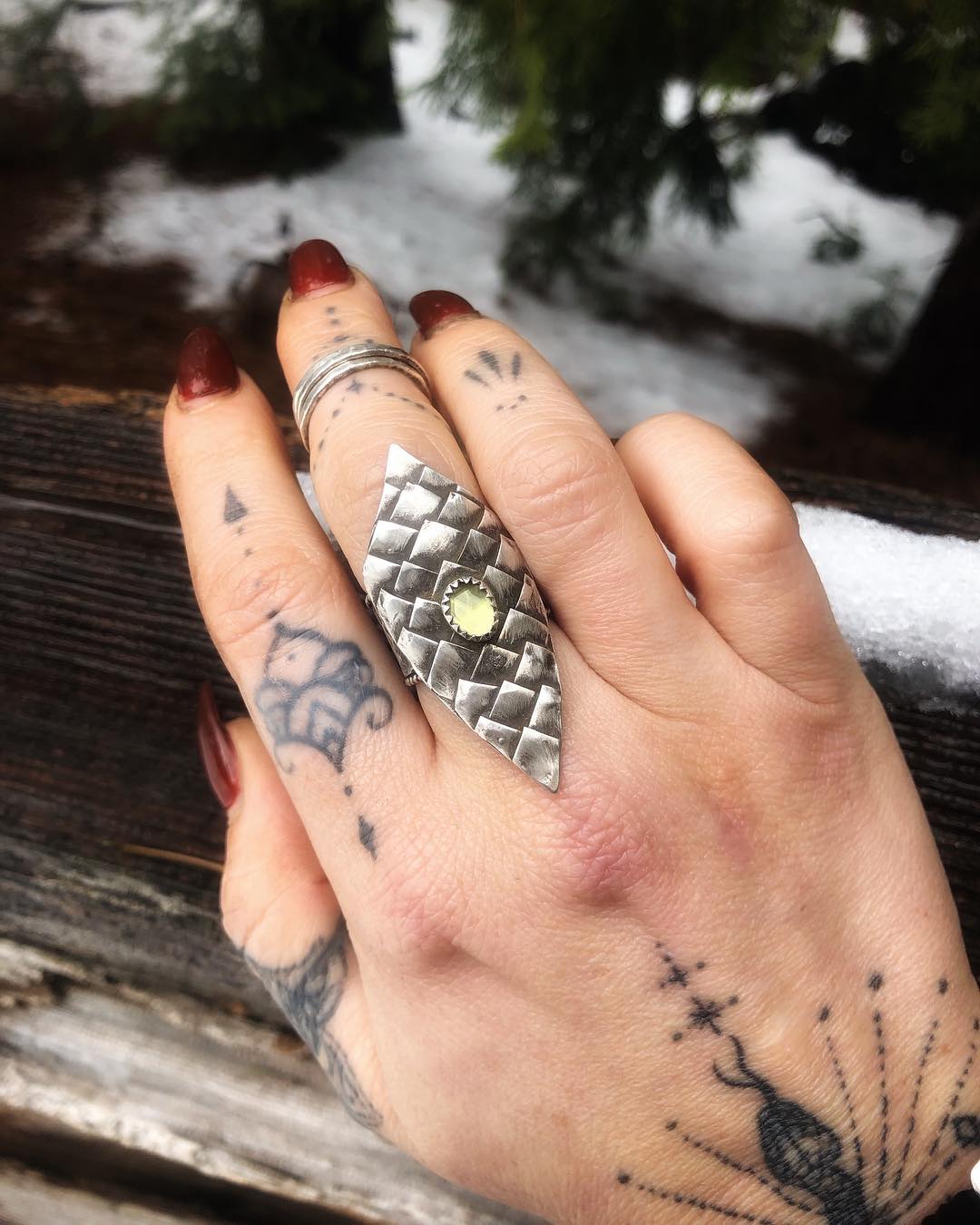 Jenna's tattooed hand wearing a wide hand-forged scale-pattern ring, against snow