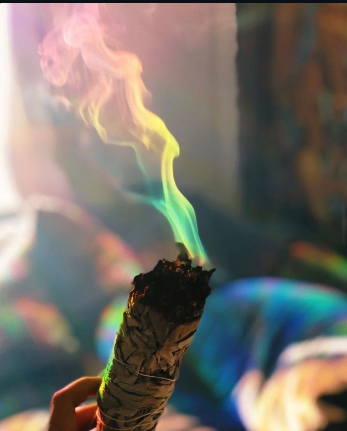 A burning smudge stick trailing rainbow smoke, held in Jenna's hand